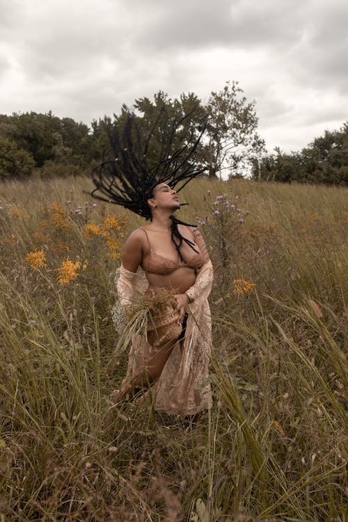 A woman standing in a meadow with her braids in motion, expressing freedom and body connection.